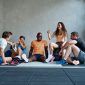 Group of young friends in sportswear talking and laughing while sitting together on the floor of a gym after a workout